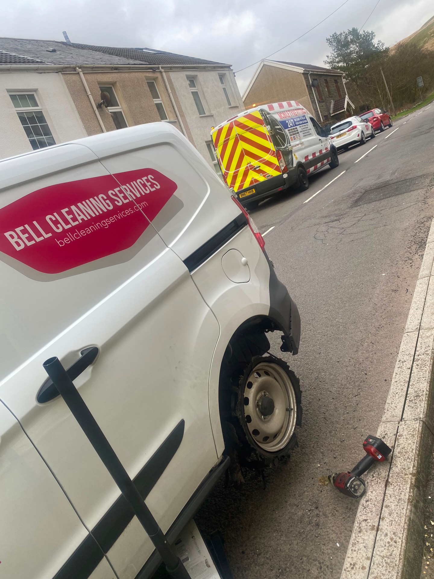 Emergency roadside tyre replacement on a residential street — shredded tyre on a work van